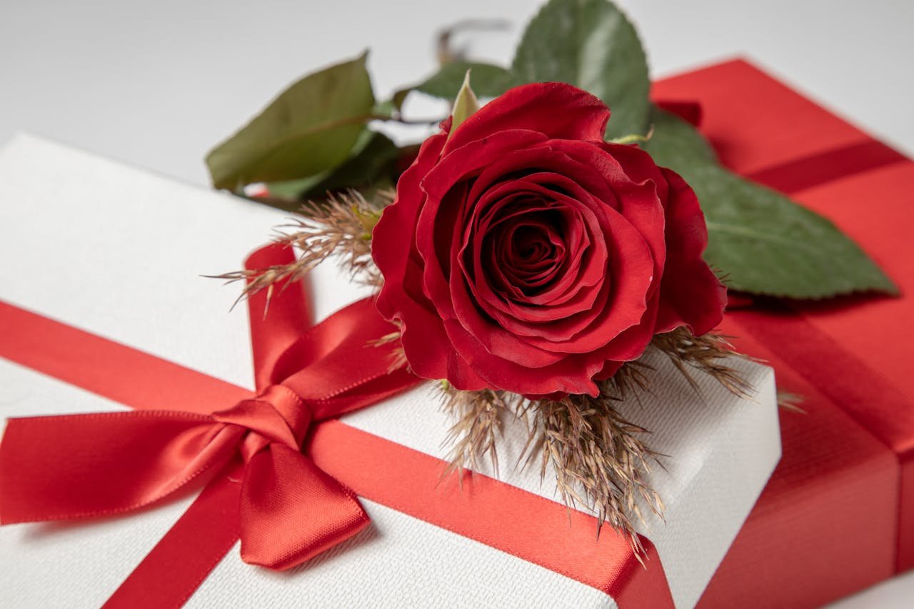 Close-up of a red rose on a white gift box tied with a vibrant red ribbon, perfect for romantic occasions.