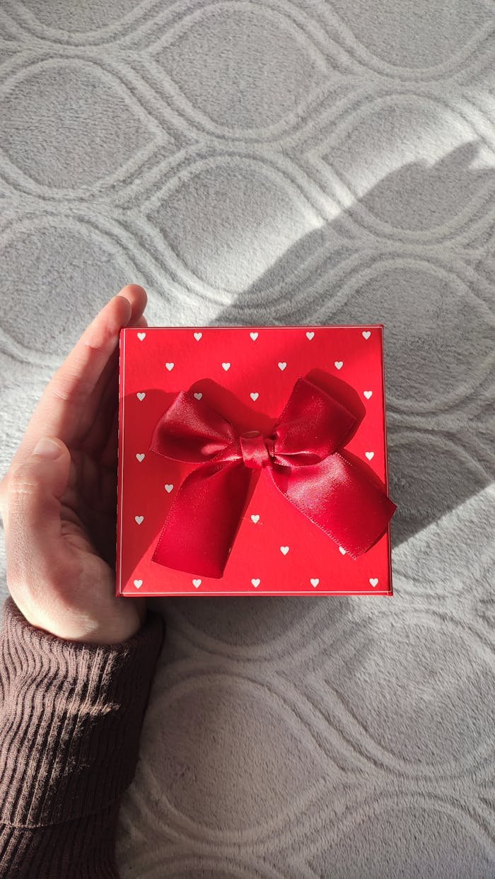 Elegant red gift box with heart patterns held in hand, perfect for Valentine's celebrations.