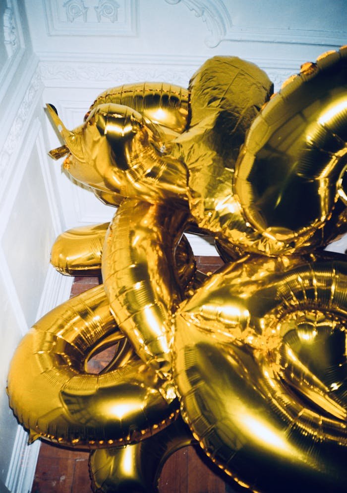 Cluster of shiny gold metallic balloons against a vintage interior wall, perfect for celebrations and parties.