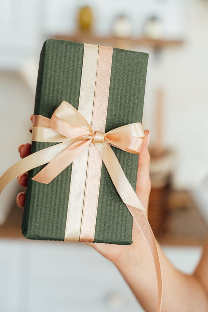 A chic green gift box wrapped with satin ribbon held by a hand, ideal for any celebration.