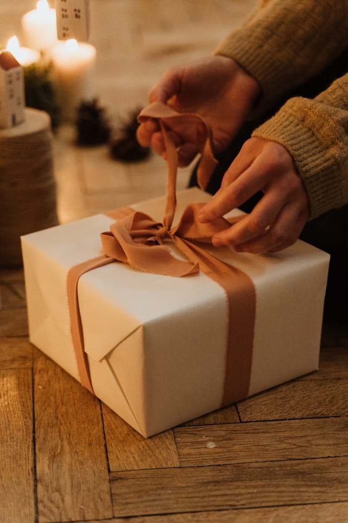 Hands carefully unwrap a gift box with a ribbon in a warm, cozy indoor setting.